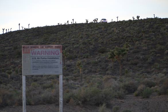 Area 51 warning sign. A white security truck can be seen on the hill overlooking the sign. Are 51 security guards are often referred to as 